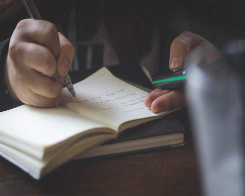 Mano escribiendo notas en un cuaderno en una cafetería
